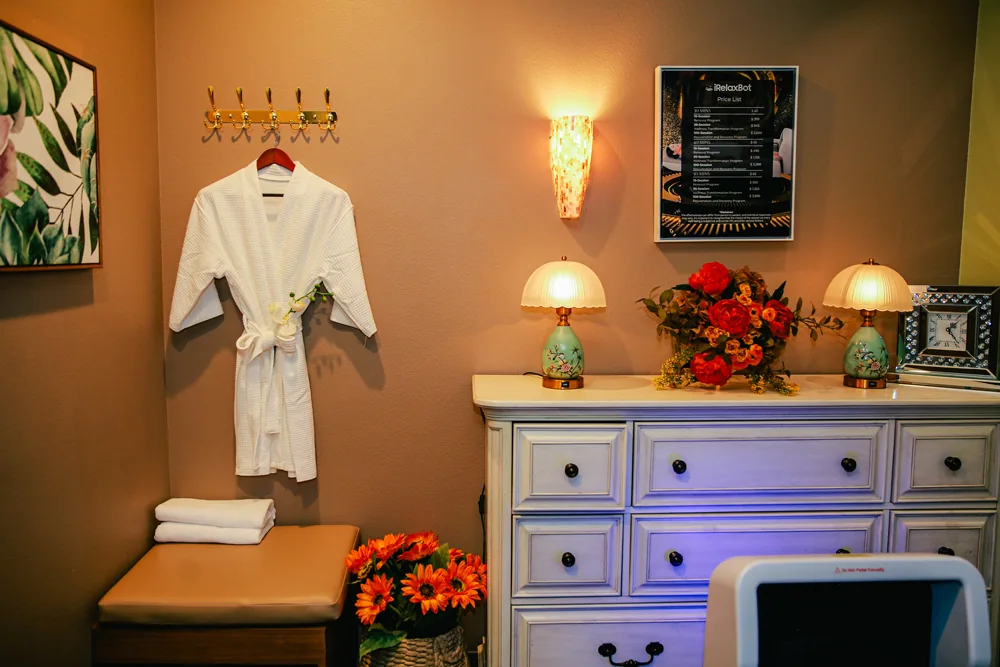 Spa robe hanging on brass hooks beside floral lamps and folded towels