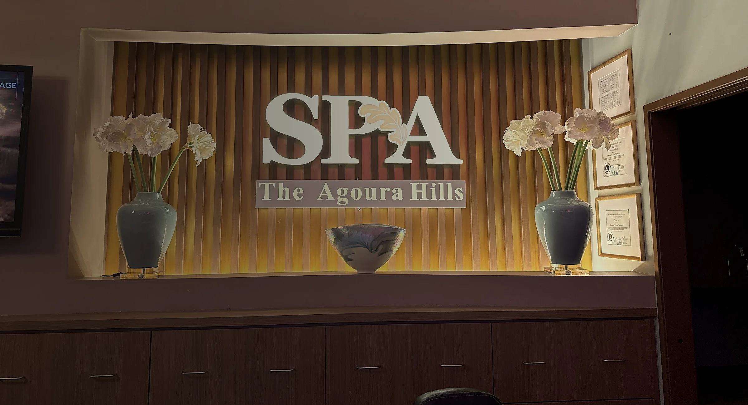 Backlit gold SPA — The Agoura Hills sign on a slatted wood feature wall with amaryllis flower vases
